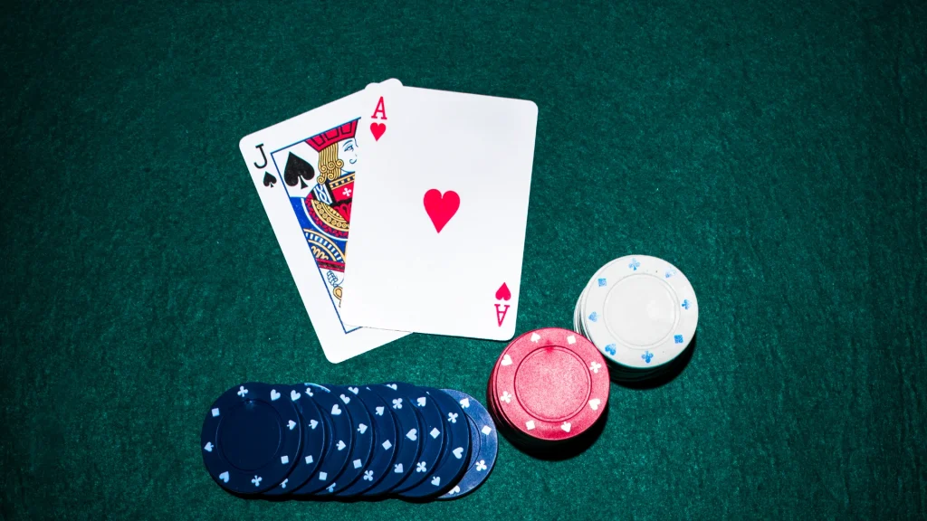 Blackjack game: Two cards, a spade blackjack and a heart ace, with casino poker chips on a green table background.